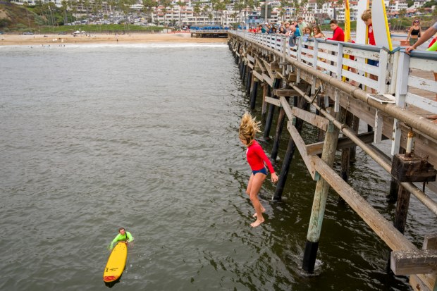 A junior lifeguard jumps off the San Clemente Pier in...